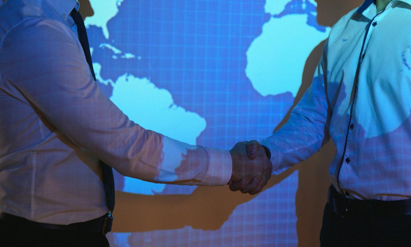 poignée-de-main-avec-carte-du-monde-en-arrière-plan-deux-hommes-d'affaires-en-arrière-plan-de-la-carte-du-monde